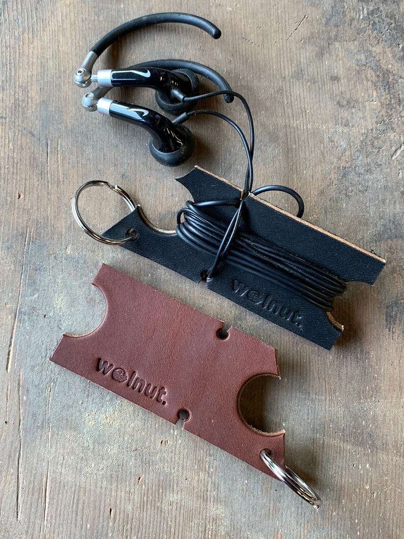 Black leather headphone holder with black headphones on a stone surface next to dark leather earbud wrap