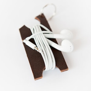 Dark brown leather earbud holder with white Apple headphones