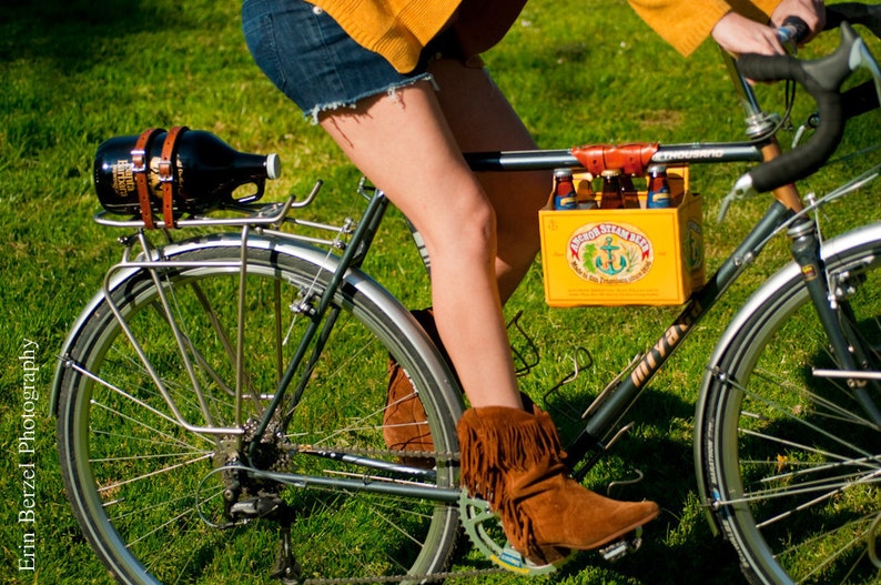 Woman riding a bicycle on grass. A yellow cardboard beer carton is attached to the top tube with the honey leather 6-pack frame cinch.