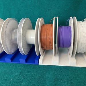 Two 3D printed filament spool holders placed side by side, each holding three filament spools, demonstrating how multiple holders can be combined for expanded storage; spools shown for display only.