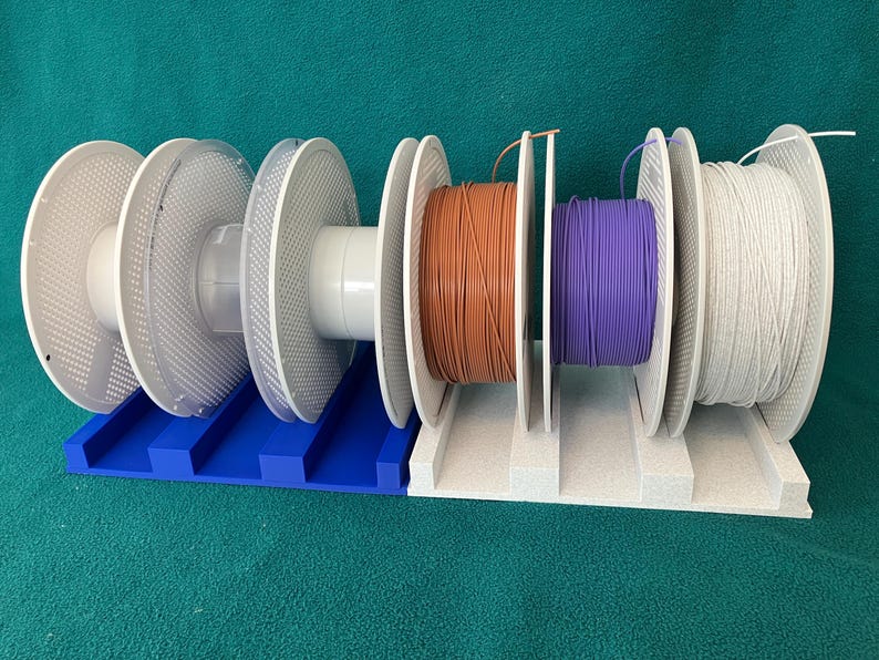 Two 3D printed filament spool holders placed side by side, each holding three filament spools, demonstrating how multiple holders can be combined for expanded storage; spools shown for display only.