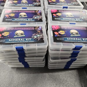 May include: A stack of clear plastic boxes with blue lids. Each box contains a mineral kit with a label that reads "Epic Fluorescents" and "Old Miners Mineral Kit". The label also states "Hand Selected Rock Minerals" and "Custom Longwave UV Mini-Flashlight Included".