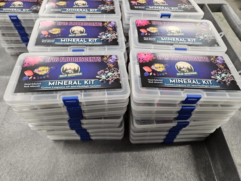 May include: A stack of clear plastic boxes with blue lids. Each box contains a mineral kit with a label that reads "Epic Fluorescents" and "Old Miners Mineral Kit". The label also states "Hand Selected Rock Minerals" and "Custom Longwave UV Mini-Flashlight Included".