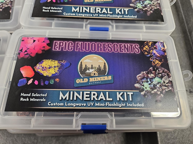 May include: A clear plastic storage box with a blue latch. The box contains a collection of rocks and minerals labeled "EPIC FLUORESCENTS" and "MINERAL KIT". The label also includes the text "Hand Selected Rock Minerals" and "Custom Longwave UV Mini-Flashlight Included".