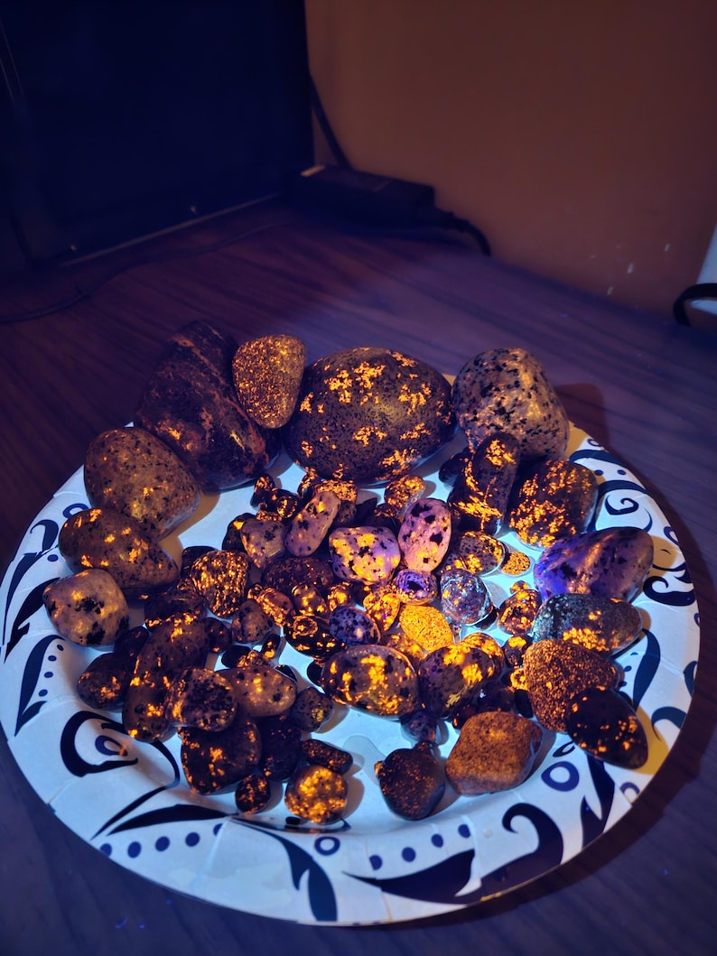 May include: A collection of polished stones with a variety of colors and patterns, including brown, purple, and yellow. The stones are arranged on a white plate with a black floral design.