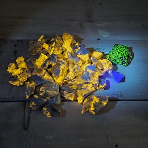 May include: A pile of yellow and blue fluorescent rocks on a wooden surface. A smaller green fluorescent rock is to the right of the pile.