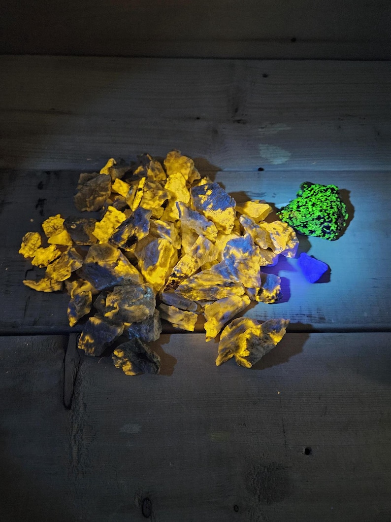 May include: A pile of yellow and blue fluorescent rocks on a wooden surface. A smaller green fluorescent rock is to the right of the pile.
