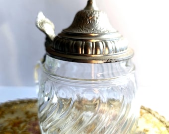 May include: A clear glass beer stein with a silver lid and a small handle. The stein has a swirl pattern and the lid has a decorative design.