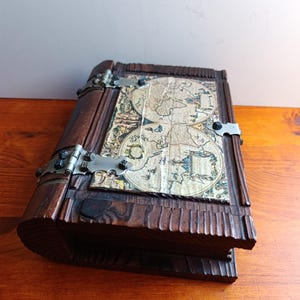 May include: A vintage wooden box with a hinged lid, featuring a detailed map design on the front. The box is dark brown with metal hinges and clasps. The map is a faded, antique style, adding to the box's historical aesthetic.