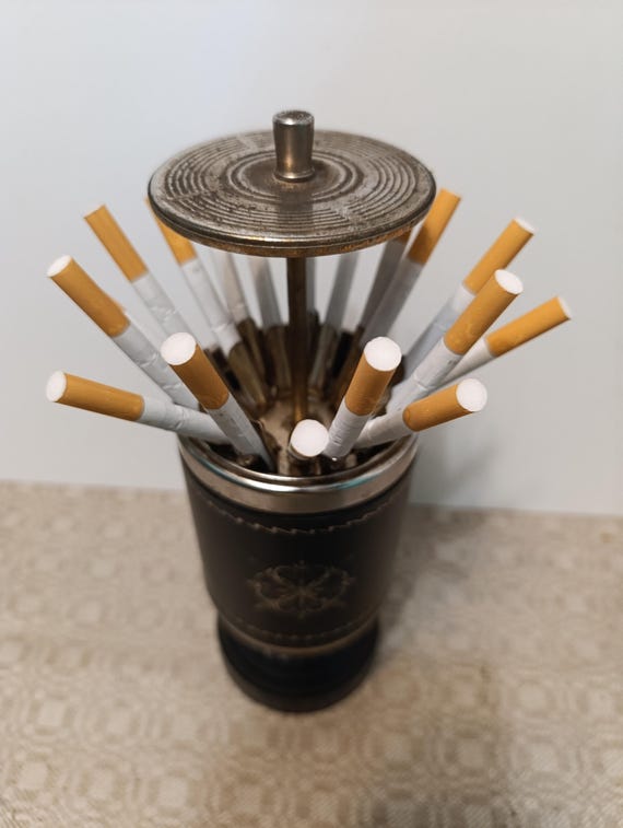 what are the old cigarette holders called Vintage, rare find cylindrical cigarette storage container with manual  mechanism. Made in Germany 1950-69s. The is called a CIGARETTE FOUNTA