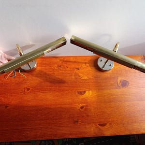 以下が含まれることがあります： 2つのヴィンテージ真鍮製ピクチャーライト。各ライトは、湾曲したアームと円形のベースを備えた、長方形のシェードを備えています。ライトは木製の表面に取り付けられています。ライトは温かみのある真鍮色です。