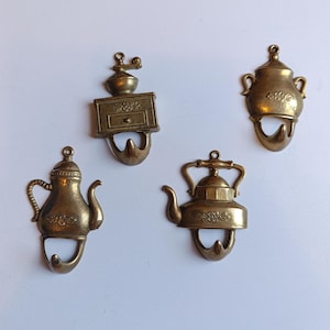 Puede incluir: Cuatro ganchos de pared de metal color latón, cada uno con un diseño diferente de temática de cocina: un molinillo de café, una olla con dos asas, una tetera con pico curvo y una hervidora. Cada pieza incluye un pequeño gancho para colgar objetos.