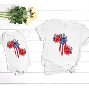 May include: White t-shirt and baby onesie featuring a design of a cartoon character with a Puerto Rican flag motif, surrounded by red hibiscus flowers and tropical leaves. The design is centered on the front of the shirts.