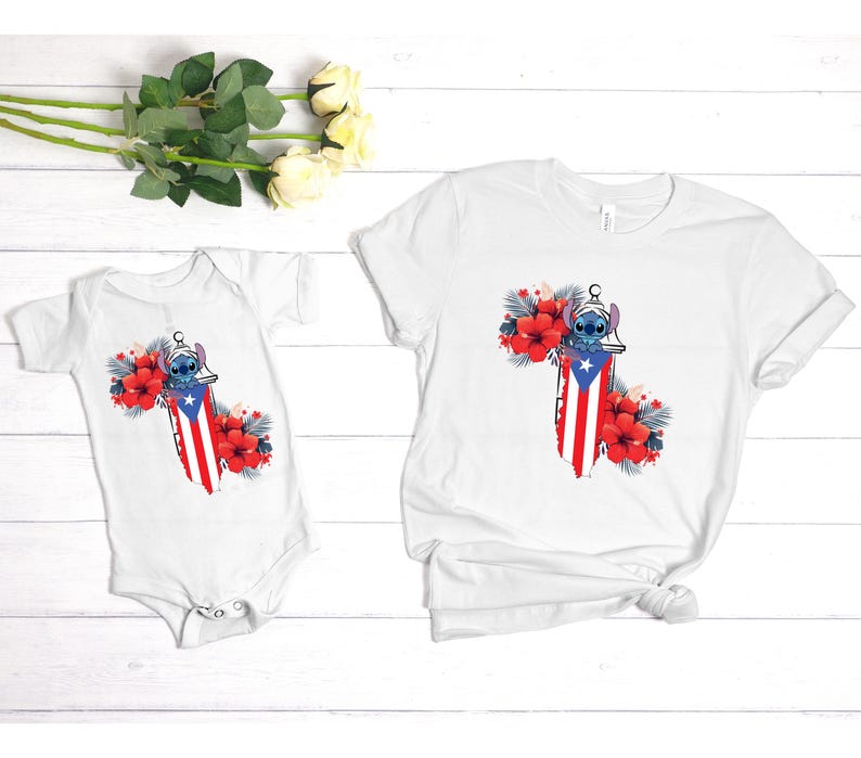 May include: White t-shirt and baby onesie featuring a design of a cartoon character with a Puerto Rican flag motif, surrounded by red hibiscus flowers and tropical leaves. The design is centered on the front of the shirts.
