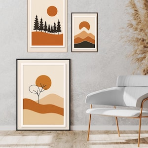 Könnte beinhalten: Drei gerahmte Kunstdrucke mit minimalistischen Landschaftsdesigns. Die Drucke zeigen eine warme Farbpalette aus Orange, Braun und Beige mit Darstellungen von Bäumen, Bergen und einer Sonne. Die Rahmen sind schwarz und braun.