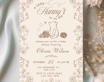 May include: Baby shower invitation with a Winnie the Pooh theme. The invitation features a beige background with brown floral accents and text. The text reads "a little Hunny is on the way!" and includes the baby shower details.