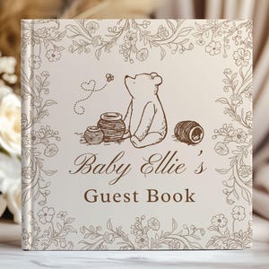May include: A square guest book with a cream-colored cover featuring a brown line-art illustration of a bear sitting near honey pots, surrounded by a floral border. The text reads Baby Ellie's Guest Book in a brown serif and script font.