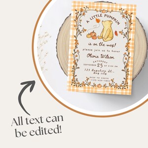 May include: A rectangular baby shower invitation card featuring a light orange and white plaid border, a central illustration of a yellow bear, pumpkins, and autumn leaves, with the text A LITTLE PUMPKIN is on the way! please join us to honor Olivia Wilson.