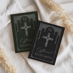 May include: Two hardback books with ornate silver cross designs. One book is dark green, the other black. Both books have the initials "KS" at the top and the word "Officiant" and the name "KYLER SMITH" in silver script.