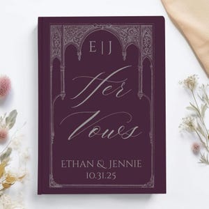 May include: A burgundy-colored wedding vow book with the words "Her Vows" in elegant script. The book features the names "Ethan & Jennie" and the date "10.31.25" at the bottom, with decorative silver accents.