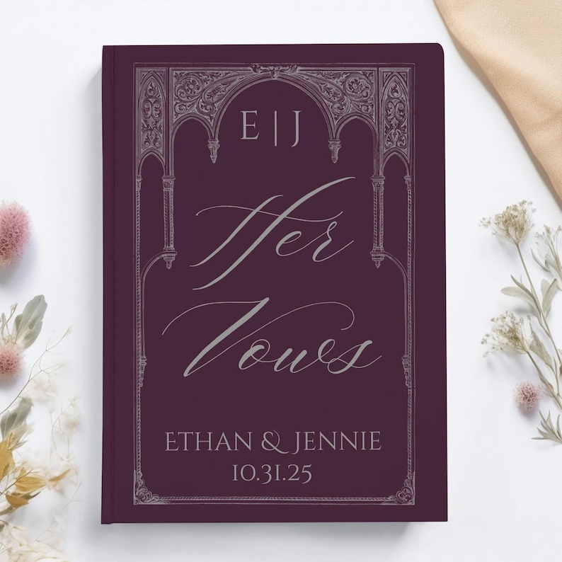May include: A burgundy-colored wedding vow book with the words "Her Vows" in elegant script. The book features the names "Ethan & Jennie" and the date "10.31.25" at the bottom, with decorative silver accents.