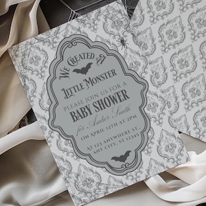 May include: Grey baby shower invitation with a damask pattern and a decorative frame. The invitation reads "We Created Little Monster, Please Join Us For A Baby Shower for Amber Smith". Features bat and spiderweb accents.