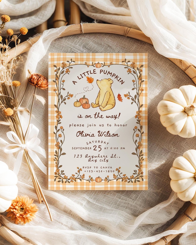 May include: A rectangular invitation card with a light orange and white gingham border. The center features a yellow bear illustration, pumpkins, and autumn leaves. Text reads: A LITTLE PUMPKIN is on the way! please join us to honor Olivia Wilson SATURDAY SEPTEMBER 25 AT 6:00 PM 123 Anywhere St., Any city RVSP TO CAHYA +123-456-7890.