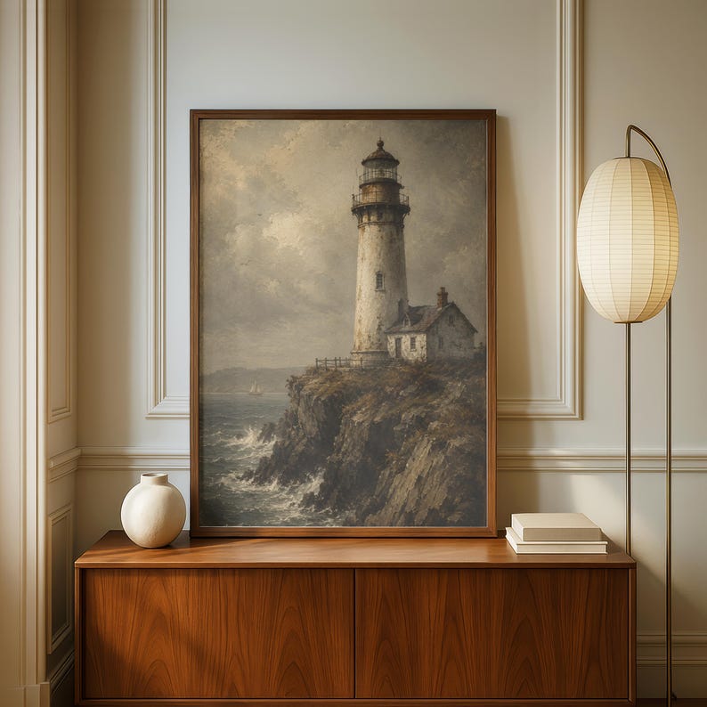 May include: A framed wall art print depicting a tall lighthouse standing on a rocky cliff overlooking a turbulent ocean under a cloudy sky. The scene features muted tones of grey, brown, and white, capturing the coastal landscape in a realistic style.