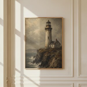 May include: A framed wall art print depicting a tall, weathered lighthouse standing on a dark, craggy cliffside overlooking a turbulent ocean. The scene features muted tones of grey, brown, and white, with a small house attached to the base.