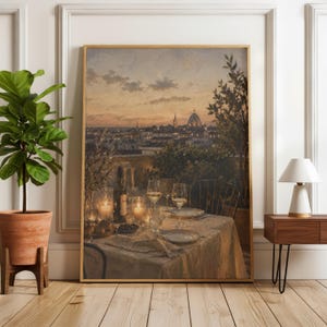 Pode incluir: Uma impress&atilde;o de arte de parede emoldurada que retrata uma paisagem urbana ao p&ocirc;r do sol com uma c&uacute;pula ao longe. O primeiro plano mostra uma mesa posta com ta&ccedil;as de vinho, uma garrafa e velas acesas sobre uma toalha de mesa branca.