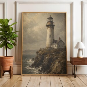May include: A framed wall art print depicting a tall, weathered lighthouse standing on a rugged cliffside overlooking a turbulent ocean. The scene features muted, earthy tones, a cloudy sky, and a small sailboat visible on the distant horizon.