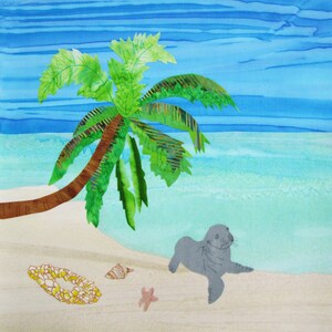 May include: A gray seal on a white sandy beach with a green palm tree and blue water in the background. There are seashells and a yellow flower lei on the sand.