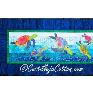 Peut inclure: Une courtepointe colorée représentant une rangée de cinq tortues marines nageant dans un océan bleu. Les tortues sont faites de différents tissus et présentent une variété de couleurs et de motifs. La courtepointe est encadrée d'une bordure bleue avec une bordure intérieure verte. Le texte "CastillejaCotton.com" est situé dans le centre inférieur de la courtepointe.