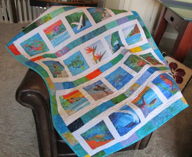 May include: A patchwork quilt featuring a grid of square fabric panels with various tropical scenes, including sea turtles, whales, flowers, and coastal landscapes, framed by white borders and vibrant blue, green, and orange patterned fabric strips.