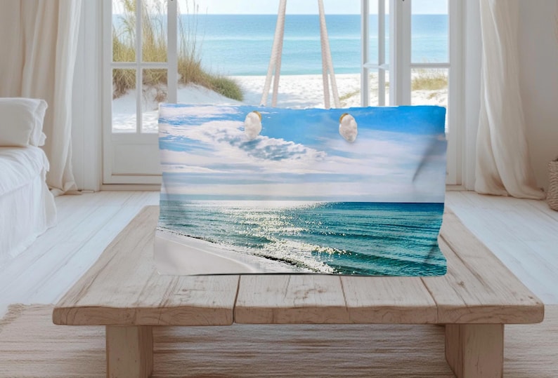 May include: A rectangular throw pillow featuring a photographic print of a sunny beach scene with turquoise ocean waves, white sand, and a bright blue sky with wispy clouds and two small white birds flying in the upper center of the image.