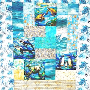 May include: A patchwork quilt featuring marine life scenes. The quilt showcases turtles, orcas, penguins, and a seal in vibrant blue, turquoise, and yellow hues. The border has a repeating pattern of turtles. The quilt is a square shape.