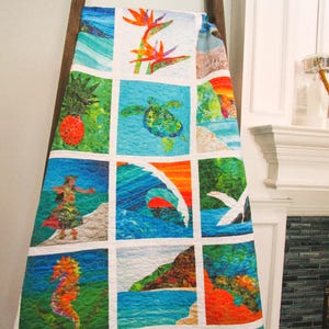 May include: A quilt featuring a grid of twelve square panels with vibrant tropical imagery, including a sea turtle, a seahorse, a hula dancer, a pineapple, a wave, and bird of paradise flowers, all separated by white fabric borders.