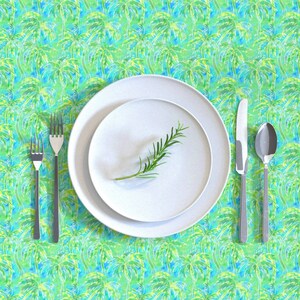 May include: A white dinner plate with a sprig of rosemary on top, set on a larger white plate. The plates are on a green and blue tablecloth with a palm tree pattern.