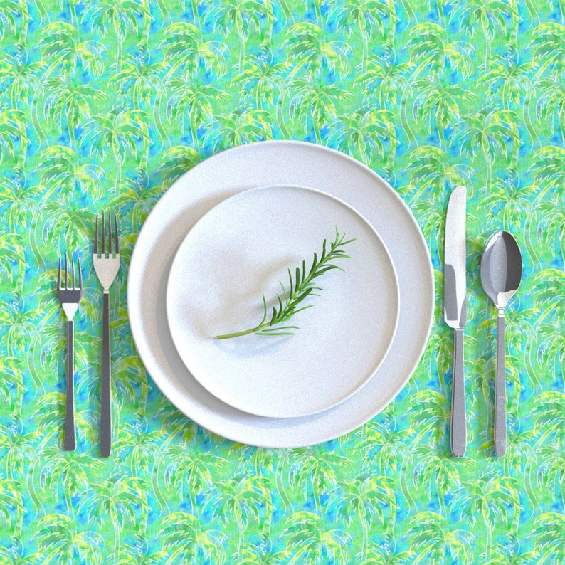 May include: A white dinner plate with a sprig of rosemary on top, set on a larger white plate. The plates are on a green and blue tablecloth with a palm tree pattern.