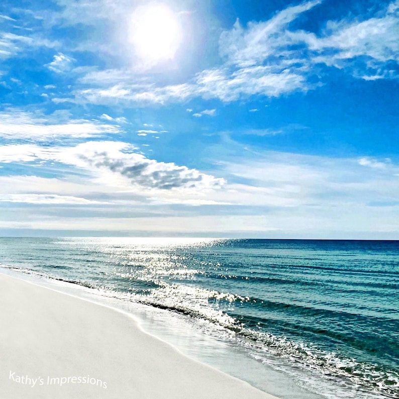 May include: A bright sunny beach scene with white sand meeting the turquoise ocean under a blue sky with scattered white clouds. The sun shines brightly above the horizon, creating a shimmering reflection on the water. Text reads Kathy's Impressions.