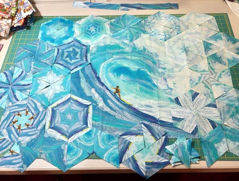 May include: A collection of fabric hexagons arranged to form a large ocean wave scene. The quilt blocks feature shades of blue, teal, and white, depicting a crashing wave with a small surfer on a yellow board in the center of the composition.
