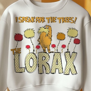 May include: White sweatshirt featuring a graphic of the Lorax character with the text "I Speak for the Trees!" and "The Lorax". The design includes yellow, orange, and red trees. The sweatshirt is hanging on a wooden hanger.