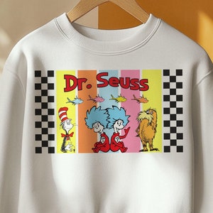 Puede incluir: Sudadera blanca con un dise&ntilde;o colorido de Dr. Seuss. El dise&ntilde;o incluye el texto "Dr. Seuss" e ilustraciones de personajes de los libros. El dise&ntilde;o est&aacute; enmarcado con un patr&oacute;n de cuadros blancos y negros.