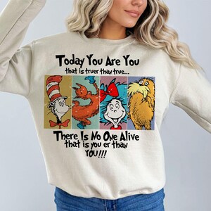 May include: Beige sweatshirt featuring Dr. Seuss characters and the quote "Today You Are You that is truer than true... There Is No One Alive that is you er than YOU!!!" The Cat in the Hat, a creature, and the Lorax are depicted.