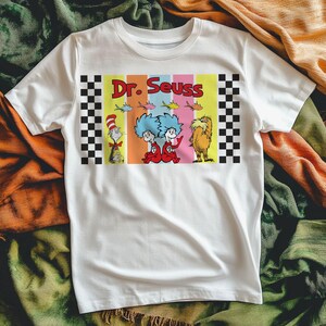 Puede incluir: Camiseta blanca con un gr&aacute;fico colorido de personajes del Dr. Seuss. El dise&ntilde;o incluye el texto "Dr. Seuss" en letras rojas, junto con ilustraciones del Gato en el Sombrero, Thing 1 y Thing 2, y el Lorax. El gr&aacute;fico est&aacute; enmarcado con patrones de cuadros blancos y negros.