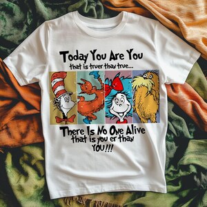 May include: White t-shirt featuring characters from a children's book. The shirt has the text "Today You Are You" and "There Is No One Alive That Is You Er Than YOU!!!". The design includes illustrations of the Cat in the Hat, a Grinch-like character, and the Lorax.