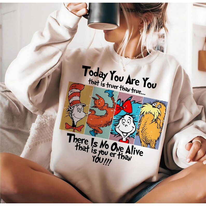 May include: Cream-colored sweatshirt featuring a colorful graphic with characters and text from a children's book. The text reads "Today You Are You" and "There Is No One Alive that is you er than YOU!!!". The graphic includes four cartoon characters.