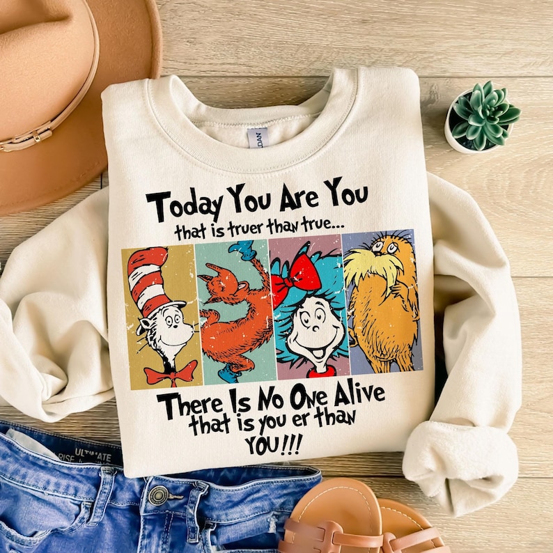 May include: Cream-colored sweatshirt featuring a colorful graphic of Dr. Seuss characters. The design includes the Cat in the Hat, a Grinch-like creature, Thing 1, and the Lorax, with the text "Today You Are You" and "There Is No One Alive that is you er than YOU!!!".