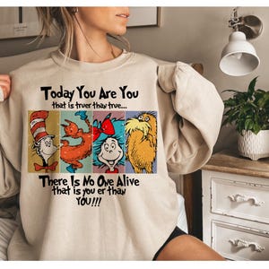 May include: Beige sweatshirt featuring a colorful graphic with characters and text from a children's book. The text reads "Today You Are You" and "There Is No One Alive that is you er than YOU!!!".
