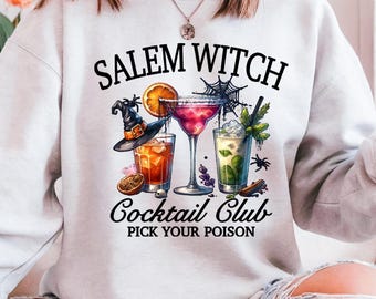 May include: A light gray sweatshirt featuring a colorful graphic of three cocktails with the text "Salem Witch Cocktail Club Pick Your Poison". The design includes a witch hat, spiderwebs, and orange slices.
